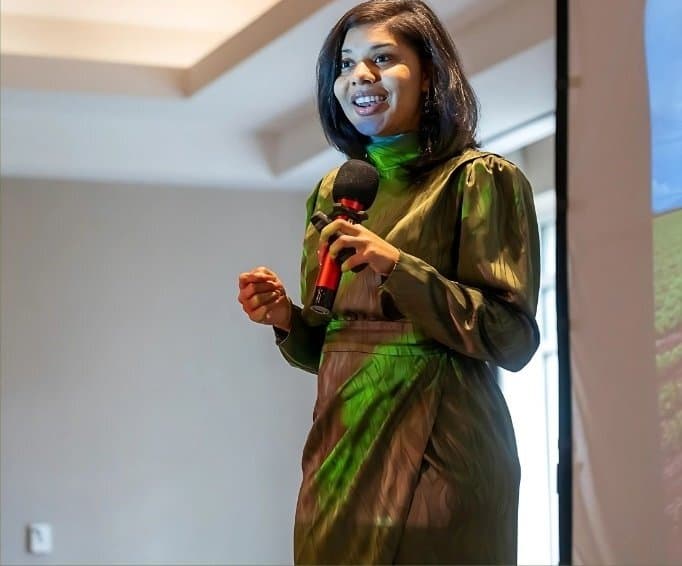 Jacqueline in a green satin dress, smiling as she speaks into a microphone.