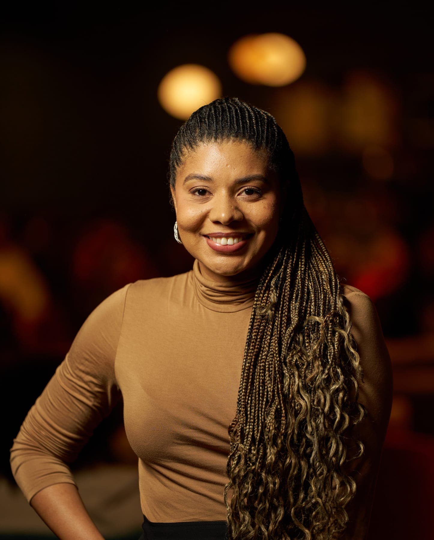 Jacqueline V. Twillie in a camel turtleneck, smiling warmly against amber light.